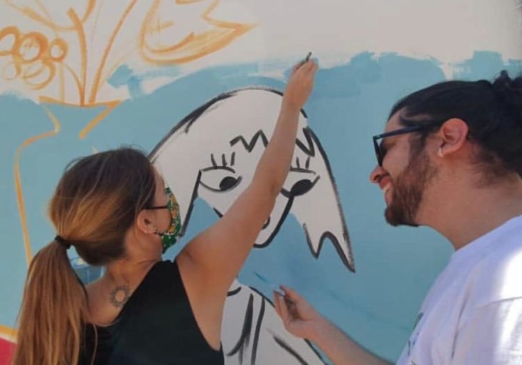 Foto de dos personas pintando detalles del mural