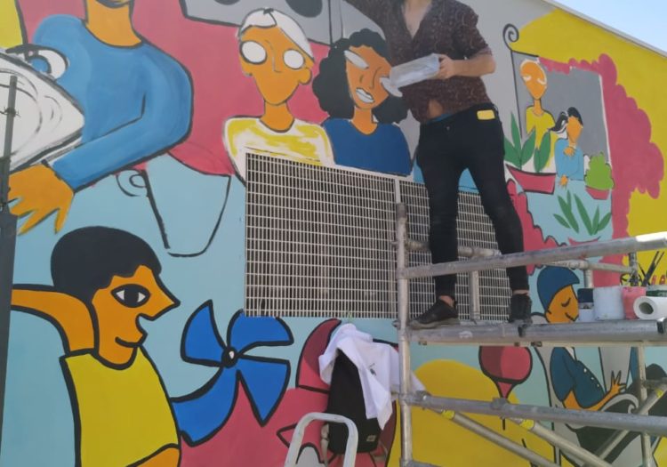 Foto de persona sobre un andamio pintando el mural